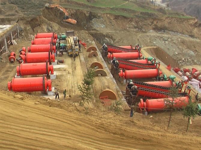 A large industrial ball mill in a mineral processing plant, showing the complex drive system and feed chutes